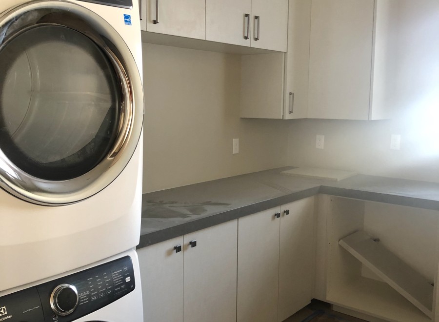 This stunning laundry room boasts modern white cabinets, sleek countertops, and high-end Electrolux washer and dryer.