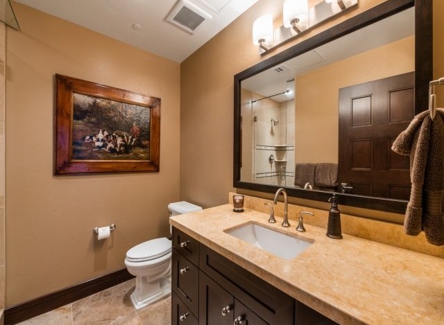 This luxurious bathroom boasts a spacious vanity with a beige countertop and dark brown cabinetry, complemented by a large framed mirror reflecting the elegant shower area.
