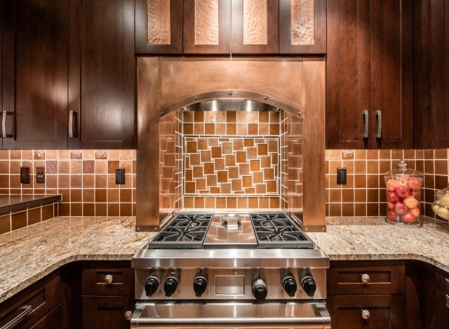 This stunning kitchen boasts a custom copper range hood, granite countertops, and rich dark wood cabinetry.
