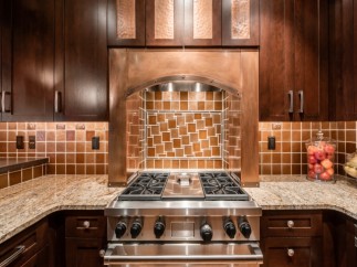 This stunning kitchen boasts a custom copper range hood, granite countertops, and rich dark wood cabinetry.