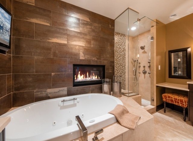Indulge in luxury with this stunning bathroom featuring a spacious soaking tub, a cozy fireplace, and a walk-in shower with multiple shower heads.