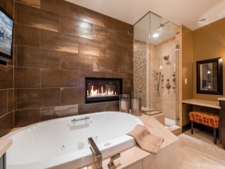 Indulge in luxury with this stunning bathroom featuring a spacious soaking tub, a cozy fireplace, and a walk-in shower with multiple shower heads.