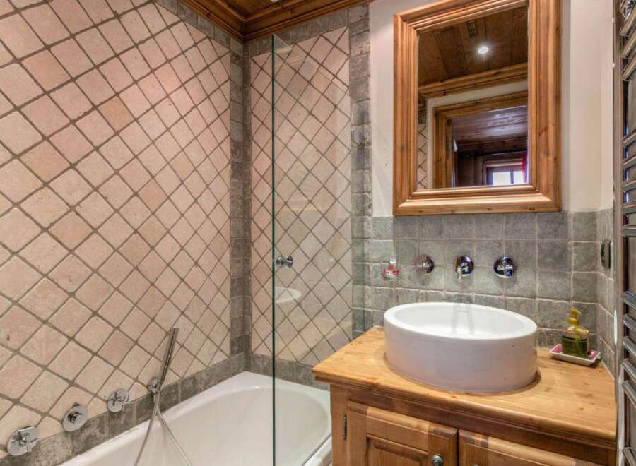 Discover the charm of this bathroom, featuring a unique tiled wall design and a stylish wooden vanity.