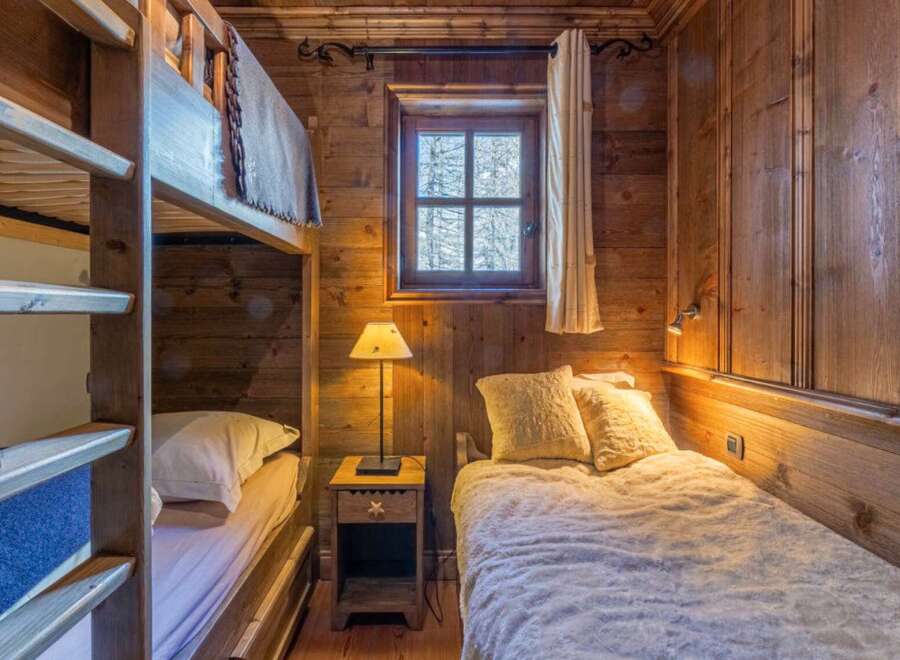 This cozy bedroom features rustic wooden walls and a charming bunk bed, perfect for a mountain getaway.