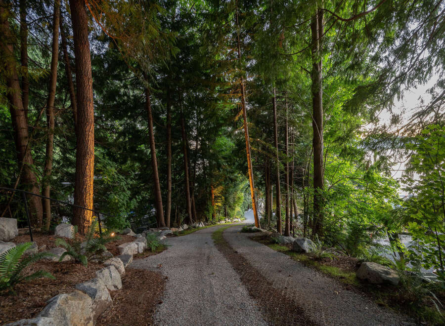 Discover the tranquility of this stunning property, featuring a winding gravel driveway that leads you through a lush, wooded landscape.
