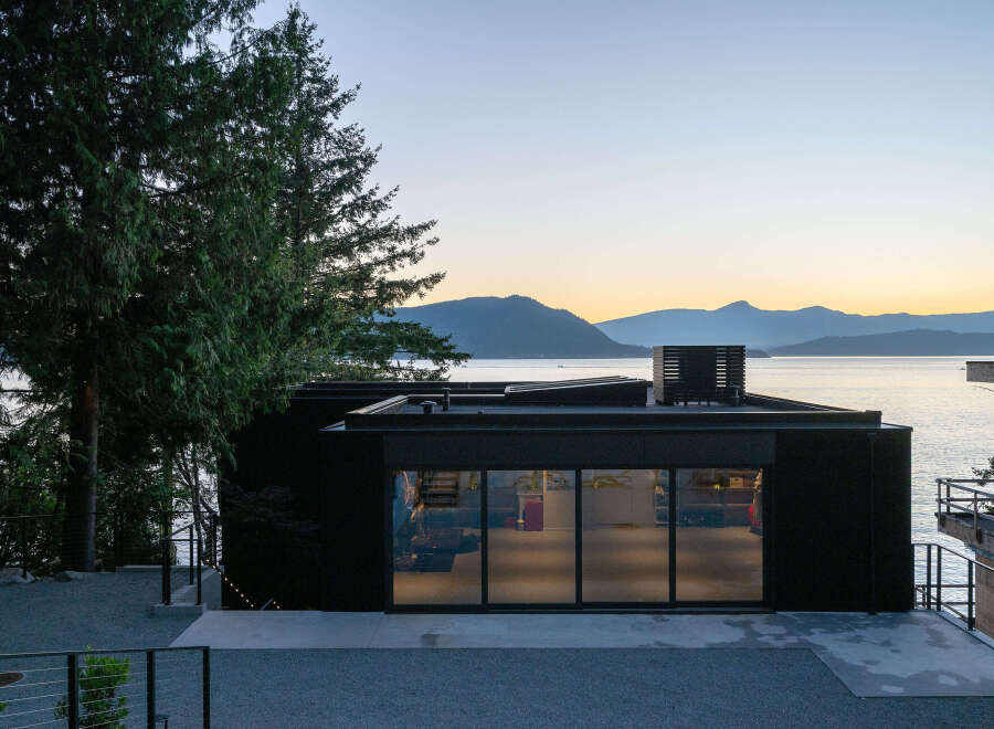 This stunning waterfront property boasts a modern, black exterior with expansive windows offering breathtaking views.