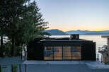 This stunning waterfront property boasts a modern, black exterior with expansive windows offering breathtaking views.