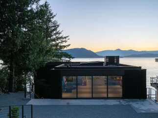 This stunning waterfront property boasts a modern, black exterior with expansive windows offering breathtaking views.