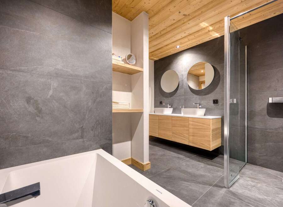 This modern bathroom features a sleek design with gray tile walls and flooring, complemented by a warm wooden ceiling.