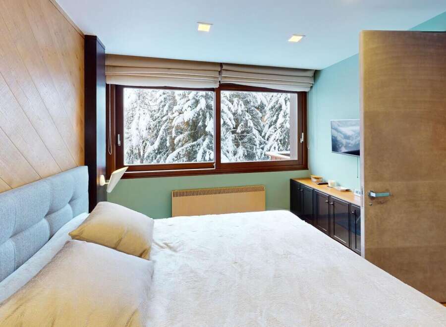 Experience the tranquility of this stunning bedroom, featuring a cozy bed and a breathtaking view of a snow-covered landscape through the large windows.