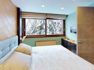 Experience the tranquility of this stunning bedroom, featuring a cozy bed and a breathtaking view of a snow-covered landscape through the large windows.