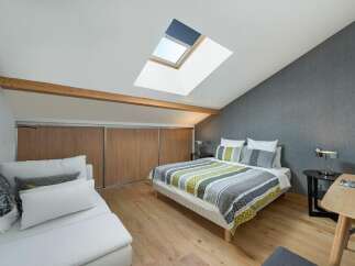 This charming bedroom features a unique design with a skylight and wooden beams, creating a bright and airy atmosphere.