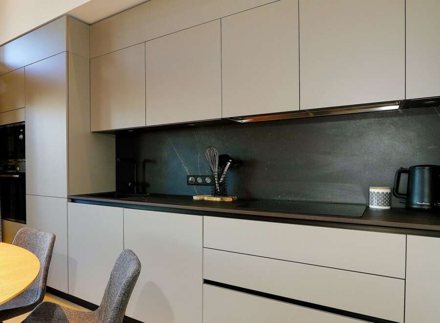 This modern kitchen boasts sleek, minimalist design with ample storage and a dark backsplash.