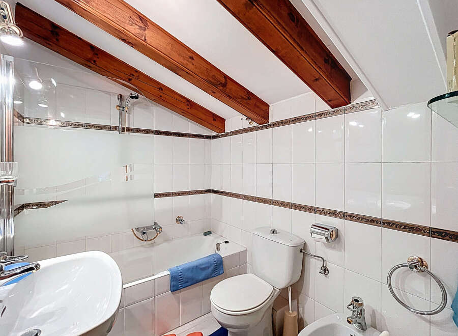 This charming bathroom features a unique design with exposed wooden beams and a slanted ceiling, creating a cozy and inviting atmosphere.