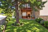 Charming stone-clad home with a welcoming wooden entrance and a balcony overlooking a lush green lawn.