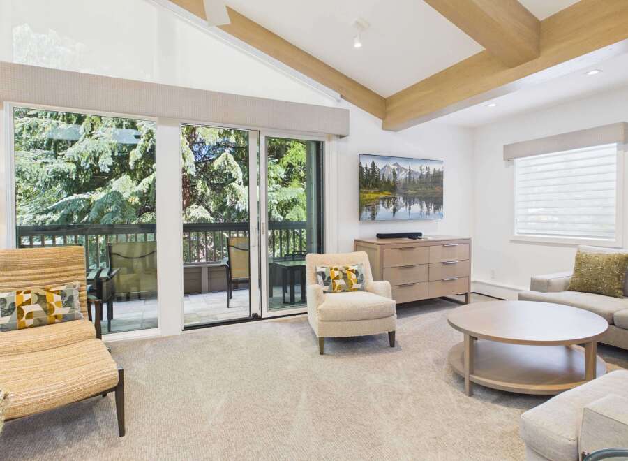 Experience luxury living in this stunning mountain retreat, featuring a spacious living area with vaulted ceilings and exposed wooden beams.