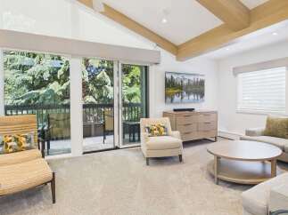 Experience luxury living in this stunning mountain retreat, featuring a spacious living area with vaulted ceilings and exposed wooden beams.