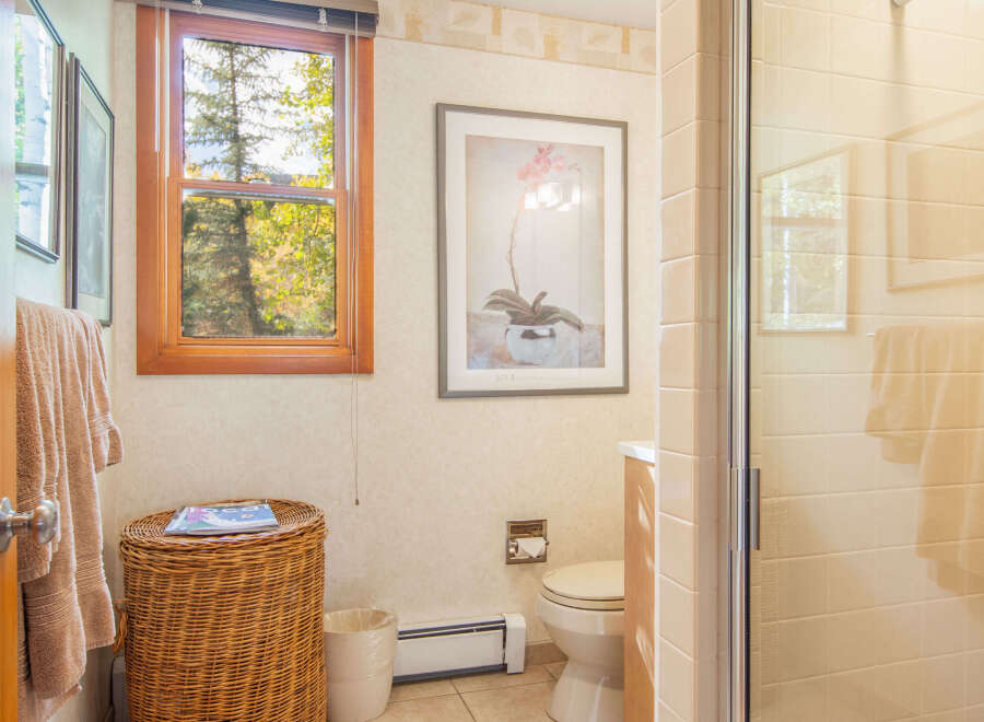 This charming bathroom features a cozy atmosphere with a wicker basket, a window with a view, and a framed artwork.