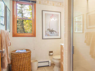 This charming bathroom features a cozy atmosphere with a wicker basket, a window with a view, and a framed artwork.