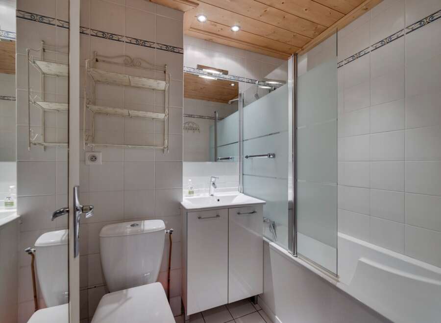 This charming bathroom features a clean and modern design with white tiles and a wooden ceiling.