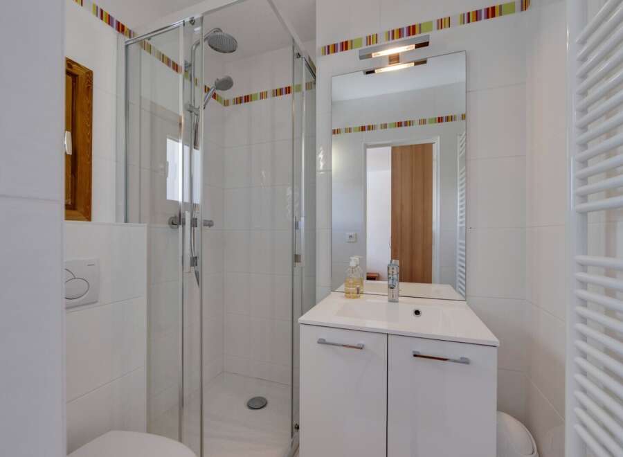 This modern bathroom features a sleek glass shower, a stylish vanity with a mirror, and a convenient toilet.