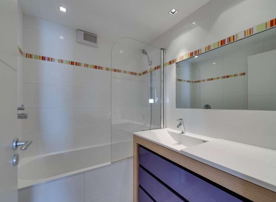 This modern bathroom features a sleek design with white tiles and a glass shower enclosure.