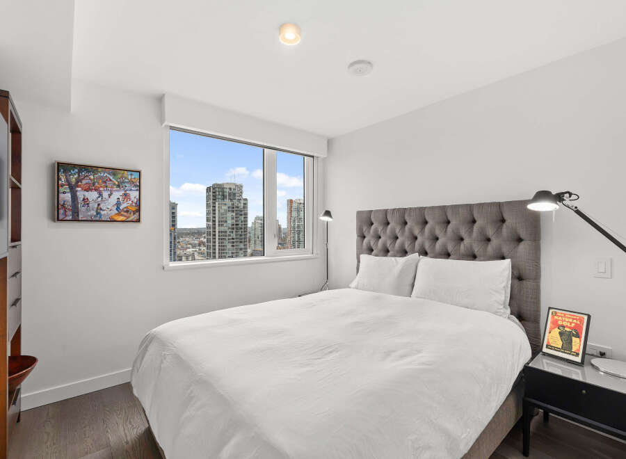 Experience luxury living in this stunning bedroom! Featuring a plush, tufted headboard, a modern bedside lamp, and a large window offering breathtaking city views.