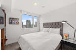 Experience luxury living in this stunning bedroom! Featuring a plush, tufted headboard, a modern bedside lamp, and a large window offering breathtaking city views.