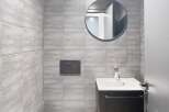 Discover this modern bathroom featuring sleek gray tiles and a stylish round mirror.