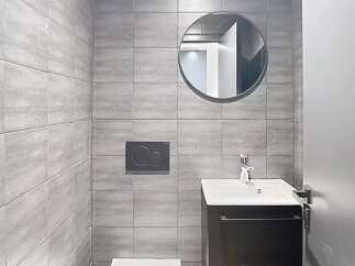 Discover this modern bathroom featuring sleek gray tiles and a stylish round mirror.