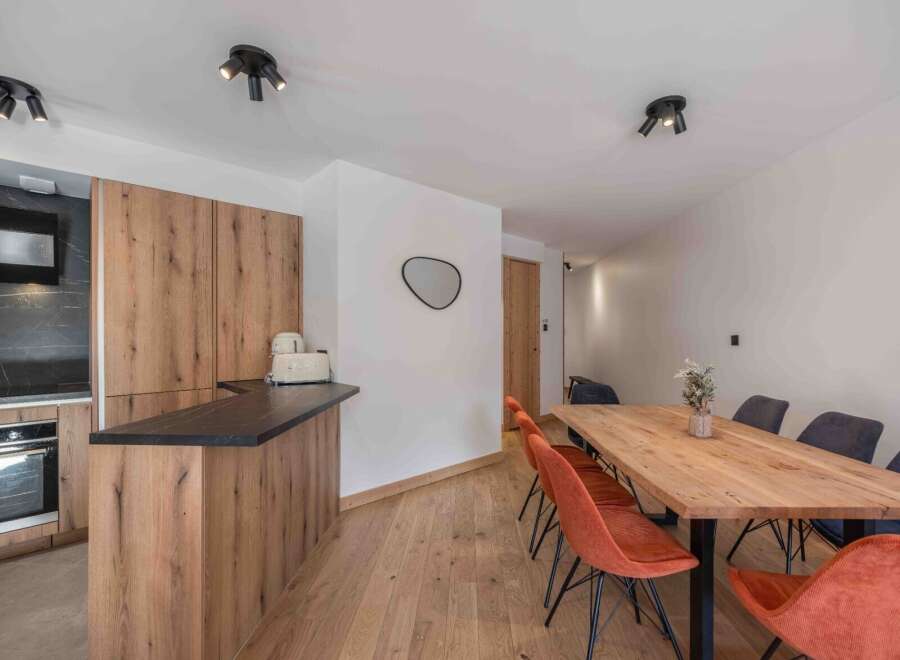 This modern kitchen and dining area boasts a sleek design with wooden cabinetry and a contrasting black countertop.