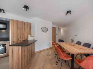 This modern kitchen and dining area boasts a sleek design with wooden cabinetry and a contrasting black countertop.