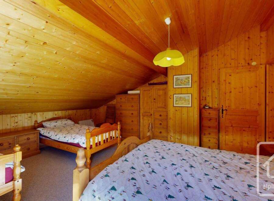 This charming bedroom features a cozy, wooden interior with a sloped ceiling, creating a warm and inviting atmosphere.
