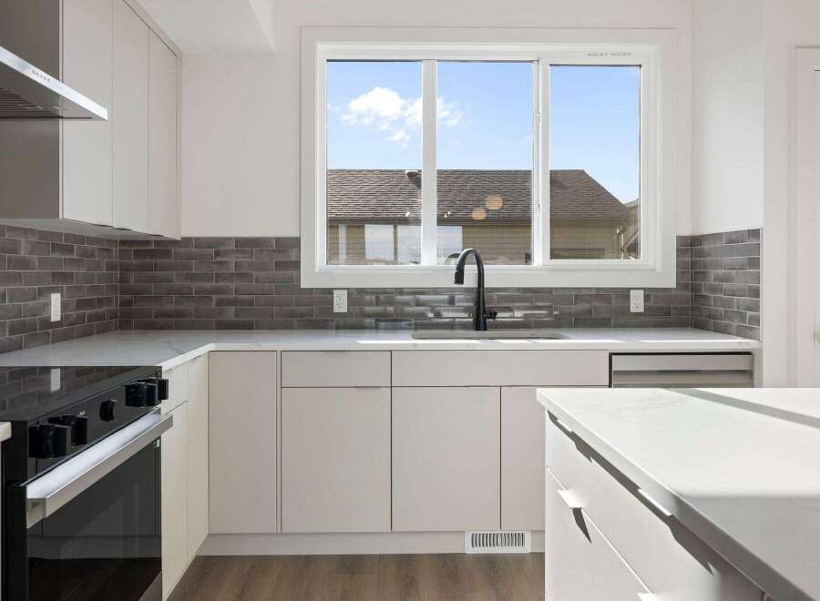 This modern kitchen boasts sleek white cabinetry, a stylish backsplash, and a stainless steel range.