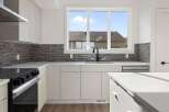 This modern kitchen boasts sleek white cabinetry, a stylish backsplash, and a stainless steel range.