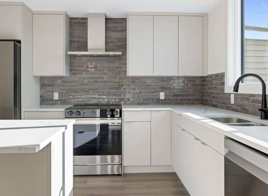 This modern kitchen boasts sleek white cabinetry and a stylish gray brick backsplash, creating a contemporary and inviting atmosphere.