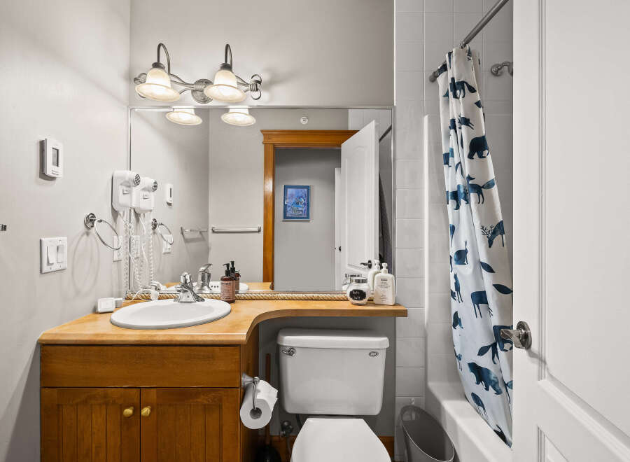 This charming bathroom features a warm wooden vanity with ample storage, complemented by a bright white sink and modern fixtures.