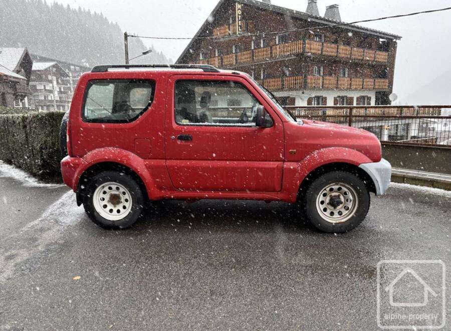 A charming red SUV is parked on a snowy street, showcasing its rugged design and compact size.