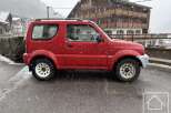 A charming red SUV is parked on a snowy street, showcasing its rugged design and compact size.