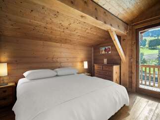 Experience rustic charm in this cozy bedroom, featuring warm wooden walls and a sloped ceiling.