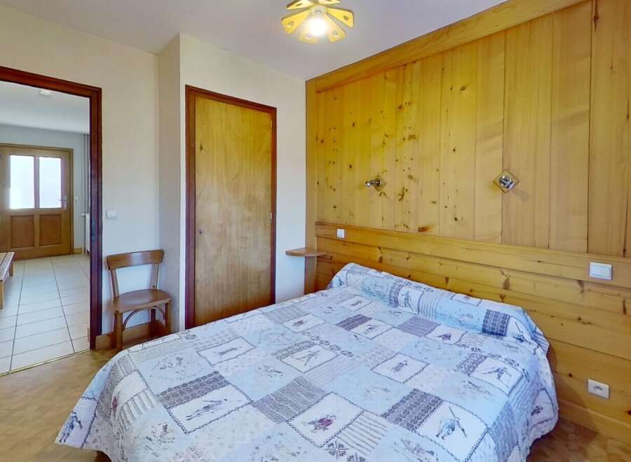 Discover the charm of this cozy bedroom, featuring a comfortable bed with a unique quilt and warm wooden paneling.