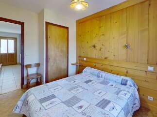 Discover the charm of this cozy bedroom, featuring a comfortable bed with a unique quilt and warm wooden paneling.