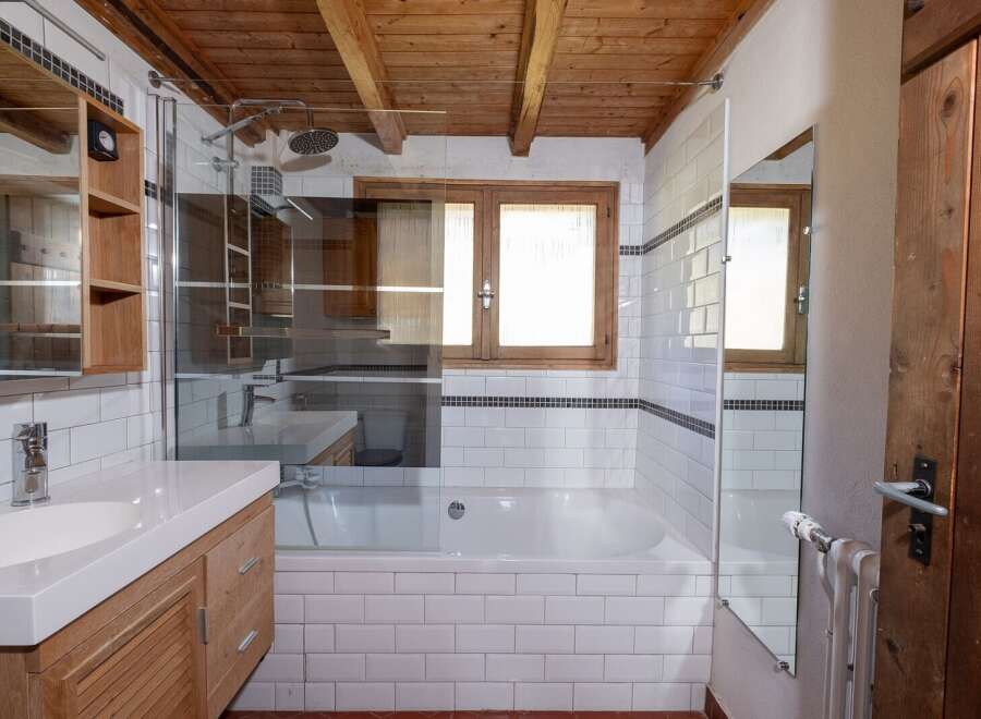 This charming bathroom features a rustic wooden ceiling and a modern white tiled design.