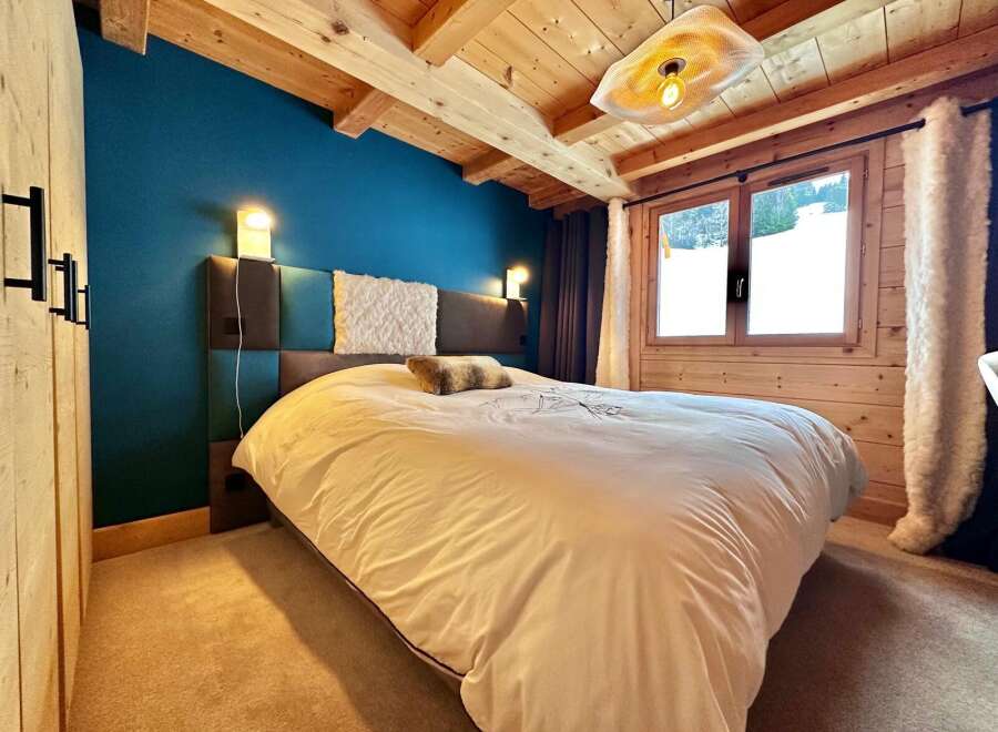 This cozy bedroom features a stunning wooden ceiling and a vibrant blue accent wall, creating a warm and inviting atmosphere.