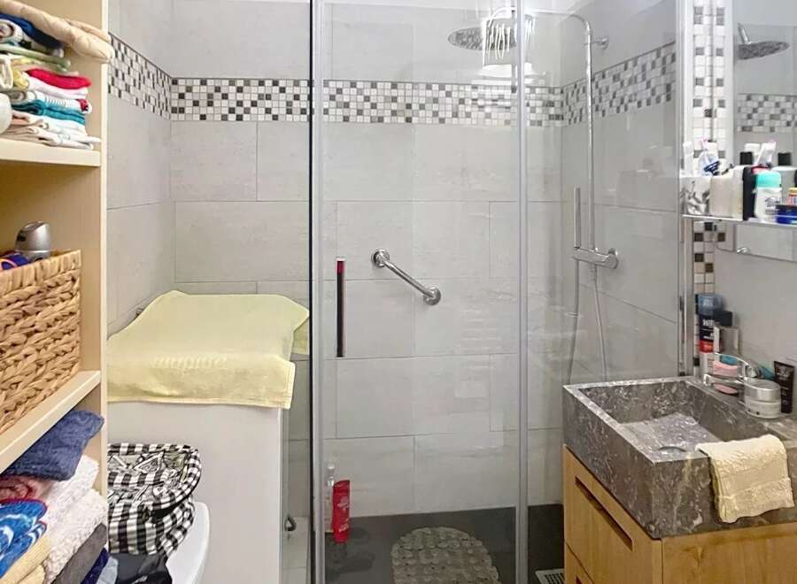 Discover this charming bathroom featuring a modern glass shower, a stylish stone sink, and ample storage solutions.