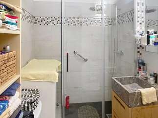 Discover this charming bathroom featuring a modern glass shower, a stylish stone sink, and ample storage solutions.