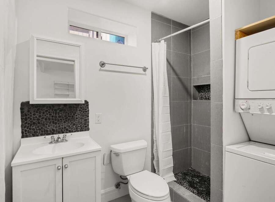 This modern bathroom features a sleek design with a gray tiled shower and a unique pebble stone accent wall.