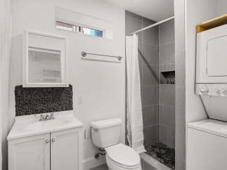 This modern bathroom features a sleek design with a gray tiled shower and a unique pebble stone accent wall.