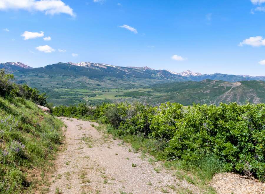 Discover the beauty of nature with this stunning property! The image showcases a scenic view of a mountain range, a dirt road, and lush greenery.