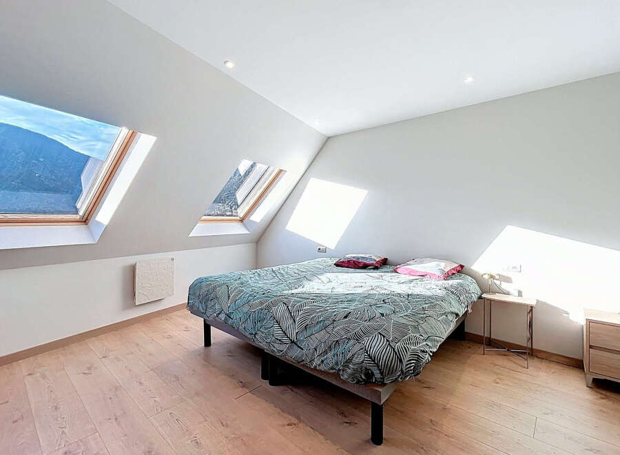 This charming bedroom boasts a unique design with its angled ceilings and skylight windows, offering stunning views and ample natural light.